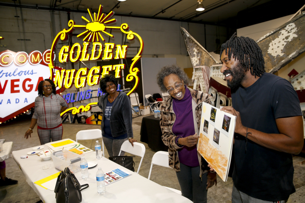 Photo of two women and a man looking at artwork in a warehouse filled with neon signage.