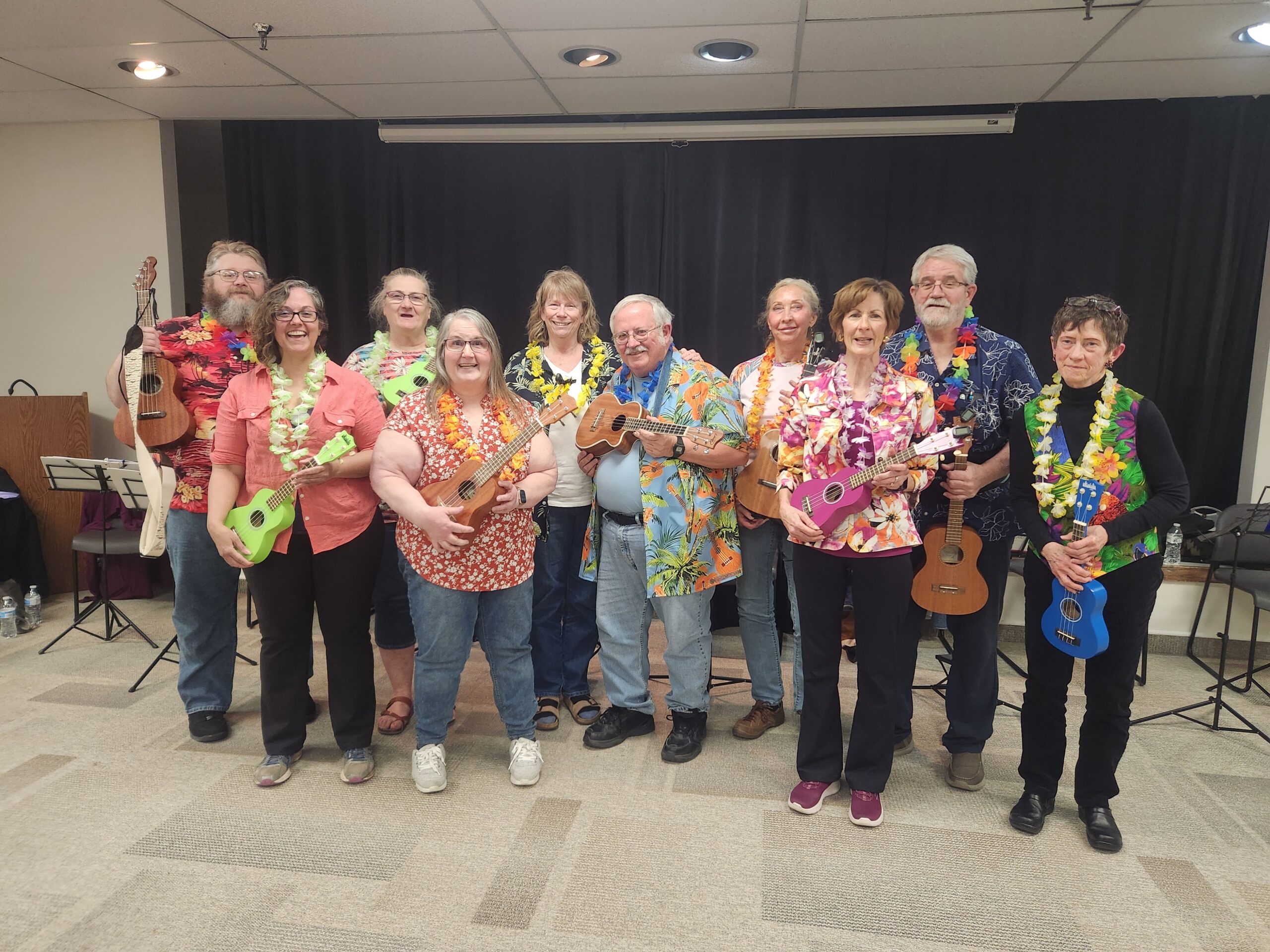 a group of creative aging students from a ukelele class stand together in Hawaiian shirts and leis, holding their instruments and smiling.