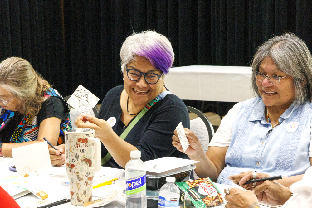 Two older women smile and create a collage.