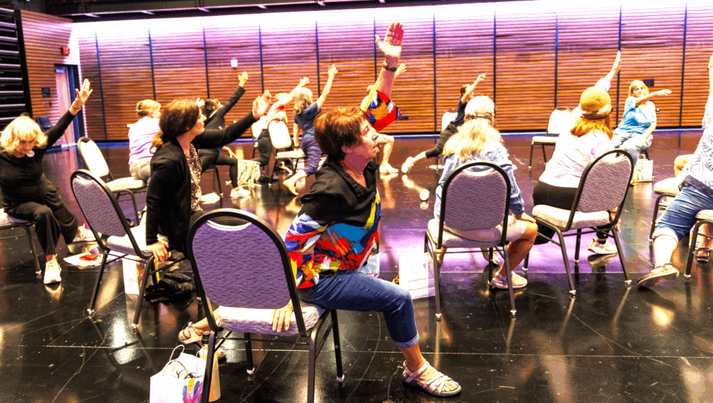 A group of older adults move their hands and legs while using chairs.