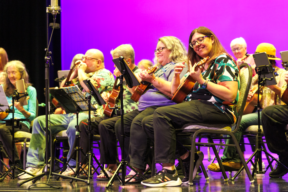 A group of older and middle-aged adults play guitar on stage.