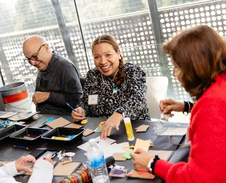 A group of older men and women sit at a table making art.