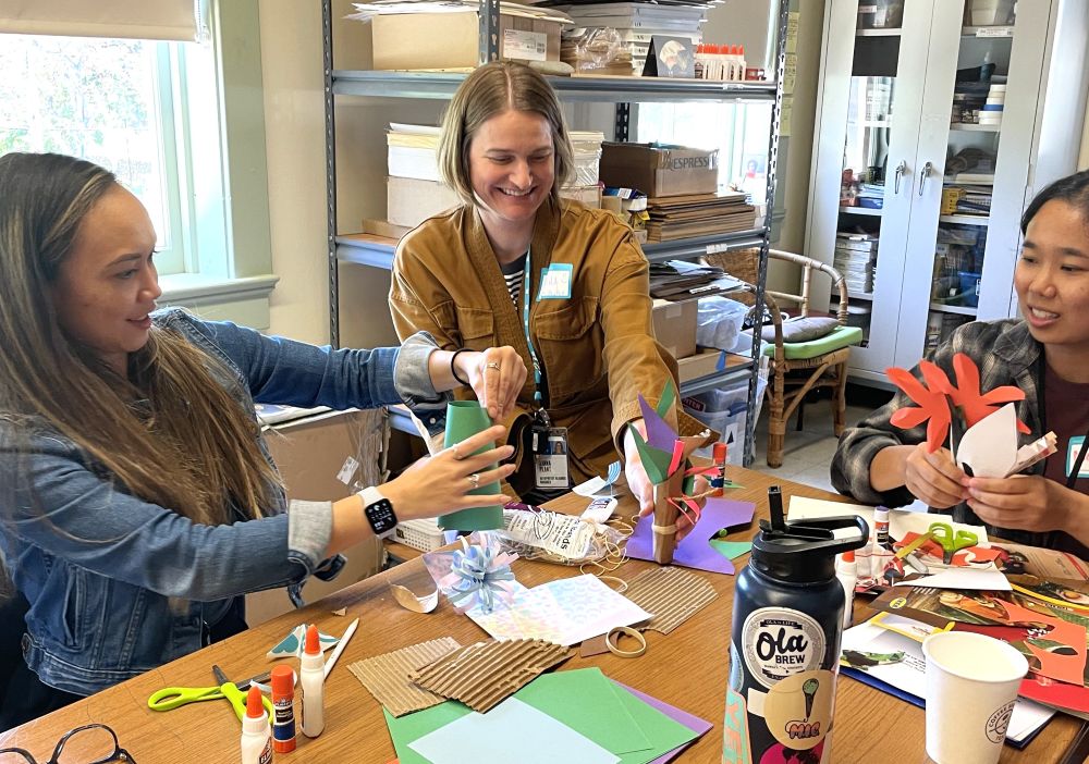 Three women who are teaching artists work on an art project together at a crafting table.