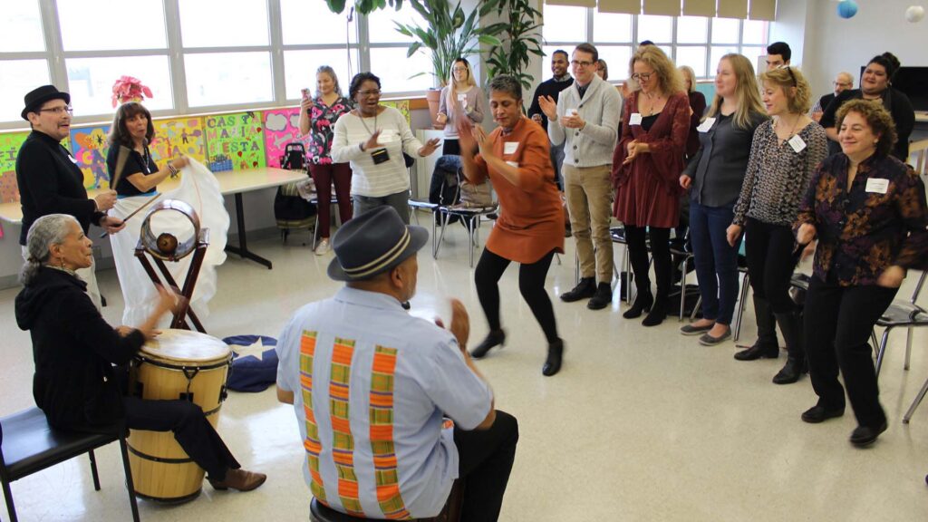 A group of older adults dance and play instruments in a spacious room with large windows.