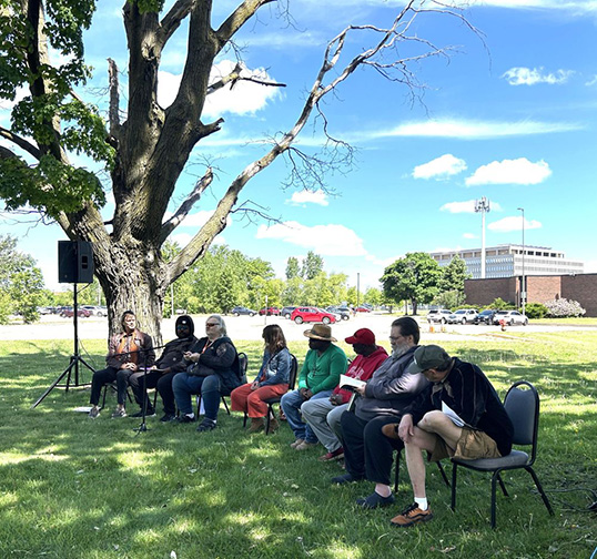 A group of veterans sit outside in chairs telling their stories.