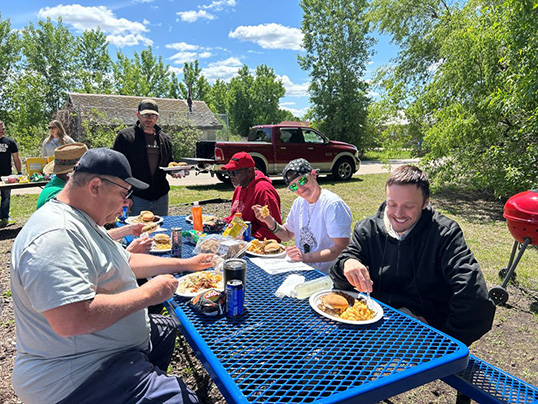 A group of veterans eat together at a picnic table outside.