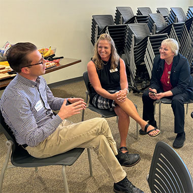 Nathan Majoros, Lifetime Arts Director of Programs, sits in a chair and talks to two other women.