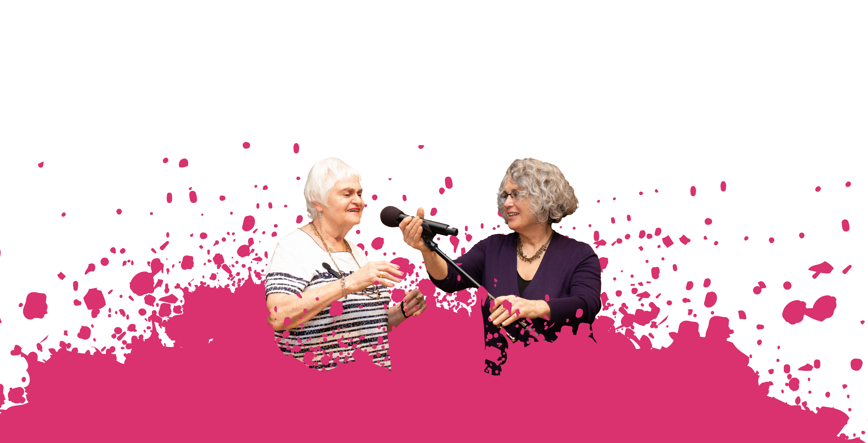 An older woman and teaching artist stand next to each other while the teaching artist holds a microphone to the older adult's face.