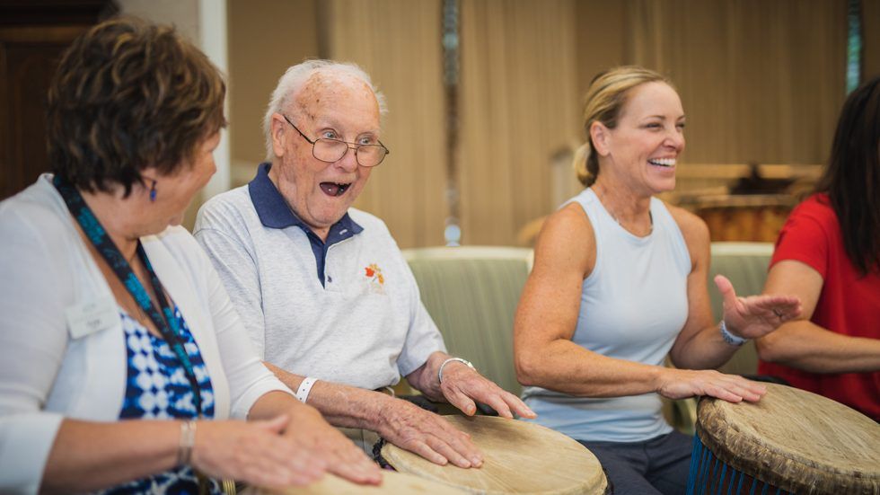 An older adult man and woman drum with a middle-aged woman while smiling.