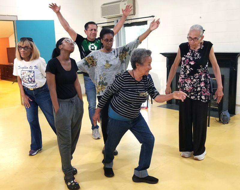 A group of older adults and teens pose and dance together.