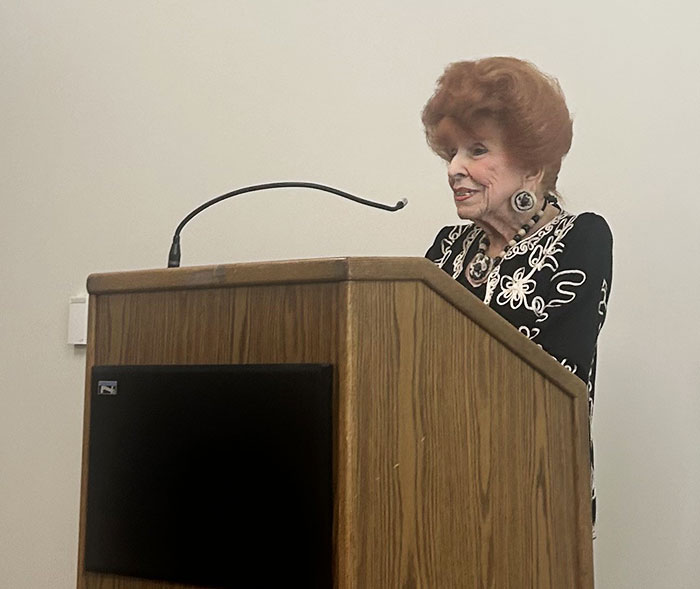 Participant, Kathy Mirrer, stands at a podium with a microphone.