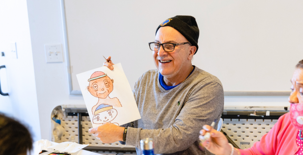 A middle-aged man smiles while holding his drawing.