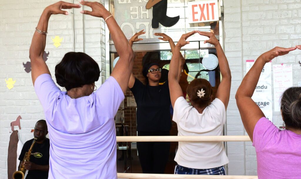 A shot of the backs of older adults practicing ballet following an instructor's' directions.