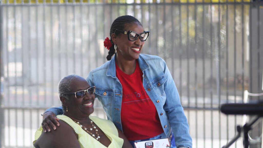 Joylynn Ross and student, Phyllis Hargrove, smile together. Joylynn is standing and has her arm around Phyllis who is sitting down.