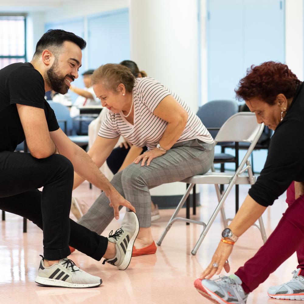 A teaching artist stretches with two older women during a dance program.