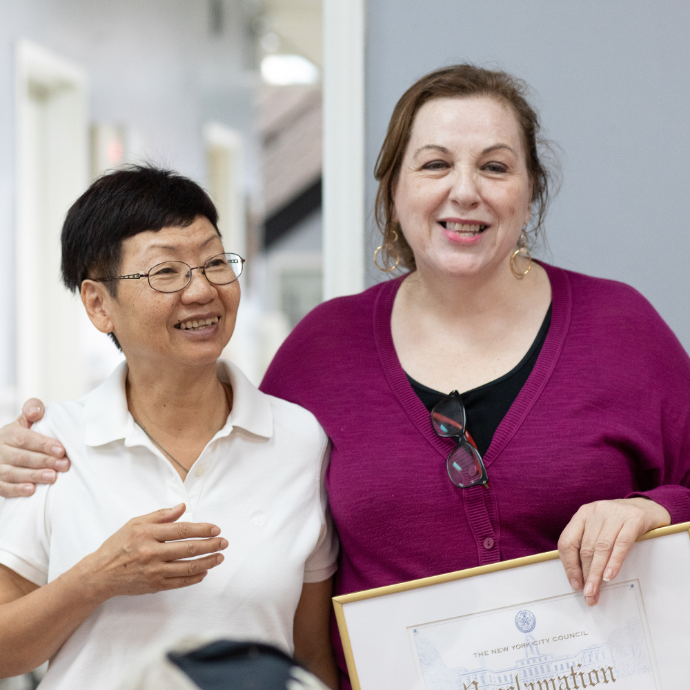 Two older woman smile while one puts her arm around the other.