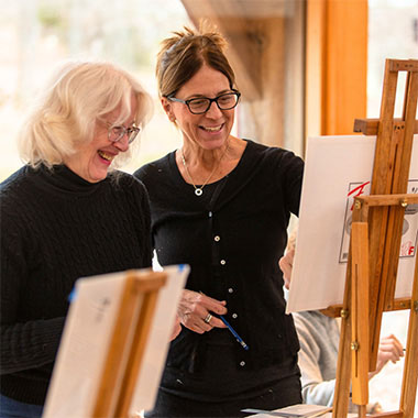 A teaching artist and older woman look at an easel together.