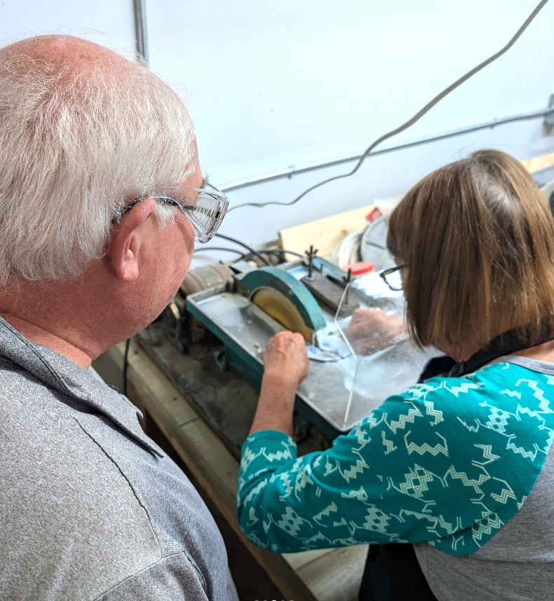 Two older adults use a table saw to work on their lapidary pieces.