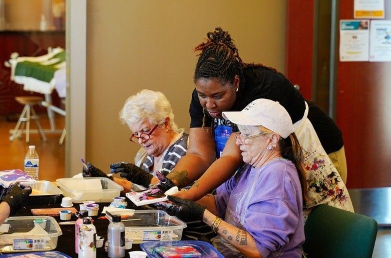 Two older adult women are being instructed by Vogue Robinson, teaching artist. 