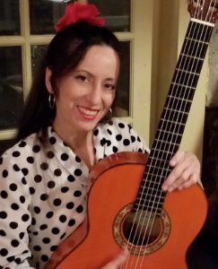 Photo of teaching artist Lisa Spraragen. She has dark hair and has a guitar in her hands. She is smiling.