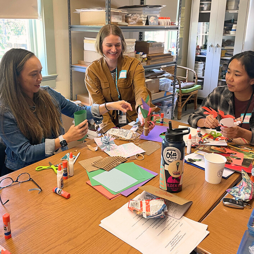 Three younger women work on an art project together at a table.