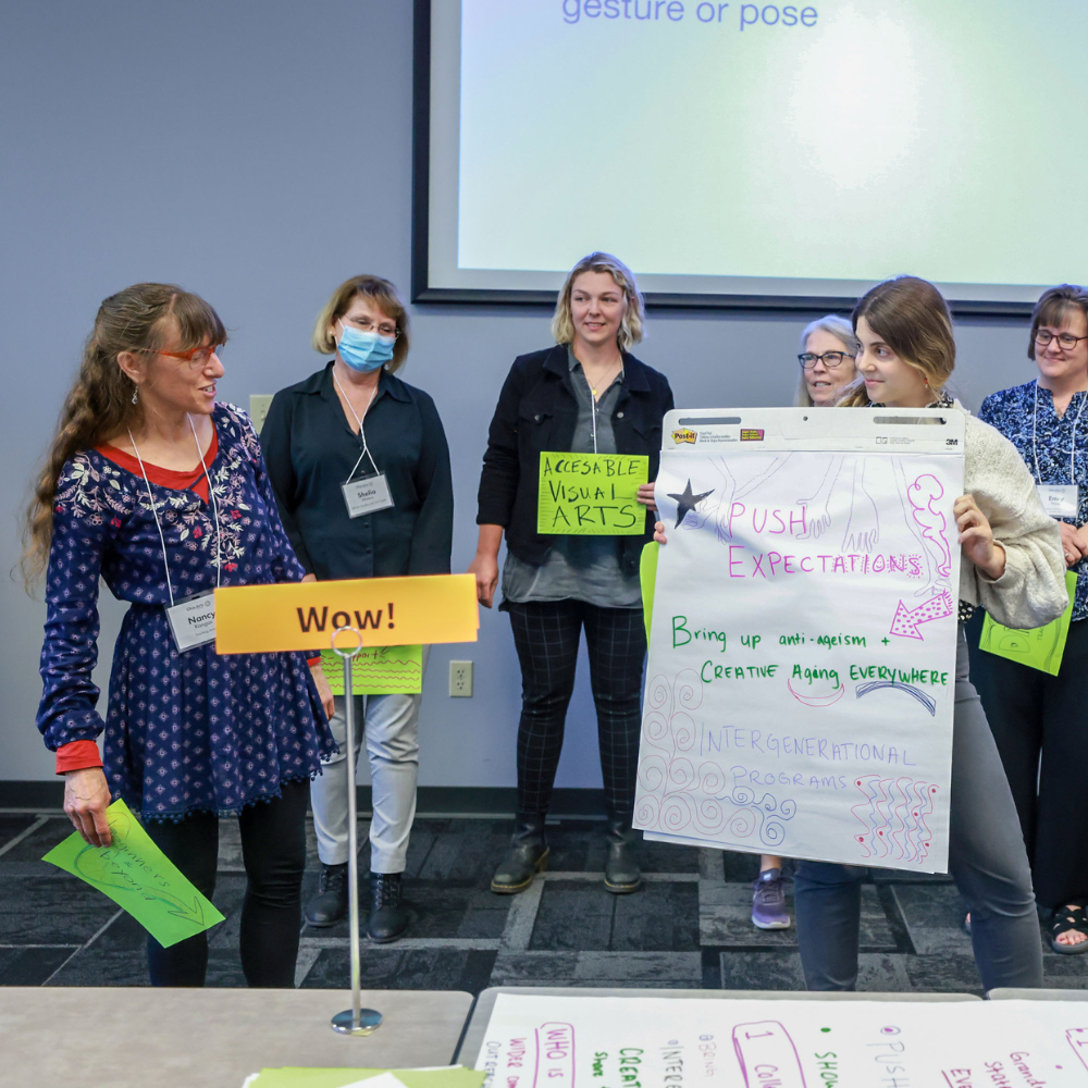 Gahlia Eden, Lifetime Arts Training and Network Manager, stands with a group of artists holding a large white paper with notes on it.