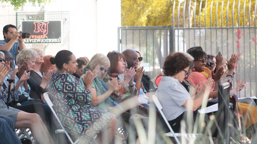 A group of culminating event attendees sit in chairs and clap and smile.